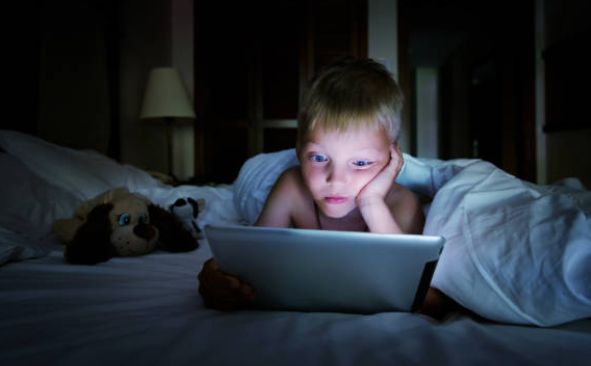Niño tumbado en la cama a oscuras mirando una tableta