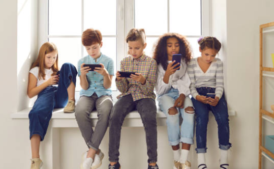 Cinco niños sentados en un alféizar, cada uno mirando su móvil