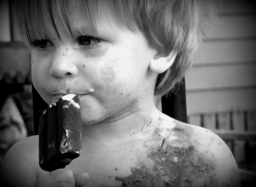 Niño pequeño comiendo un polo, con la cara manchada, en blanco y negro