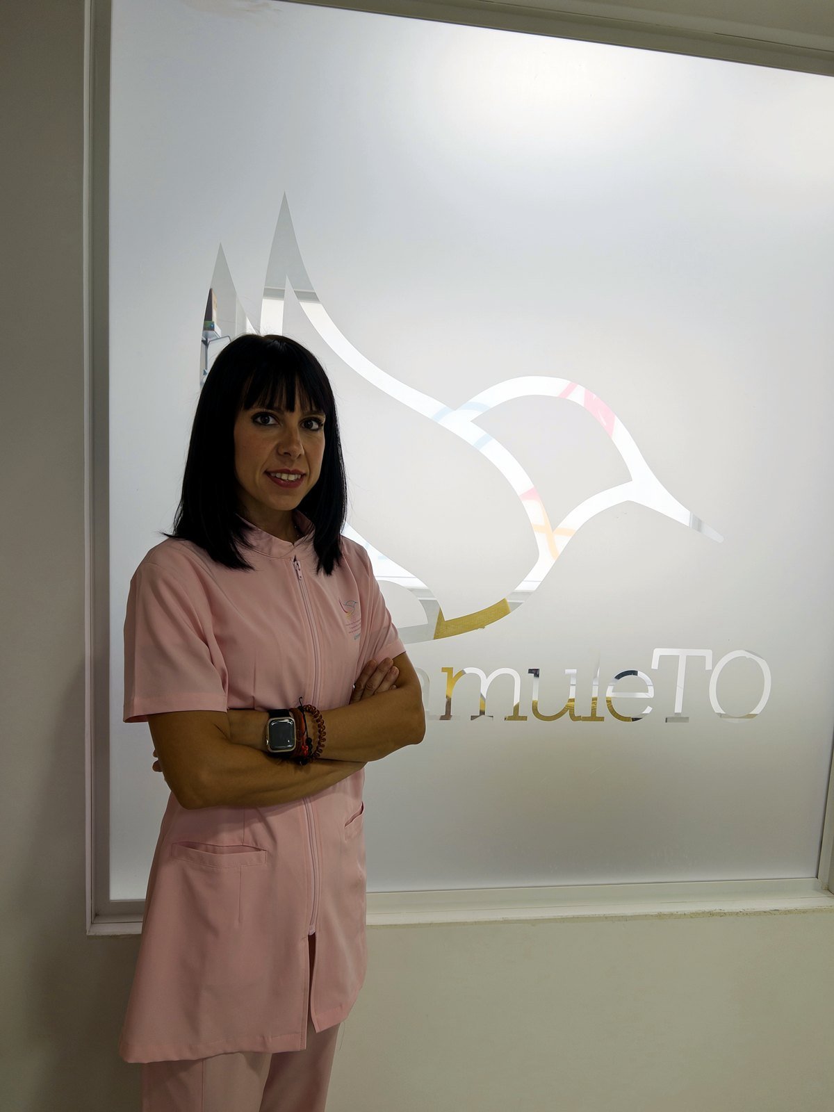 Laura Ortega, con el uniforme de amuleTO, ante el cristal con el logotipo del centro