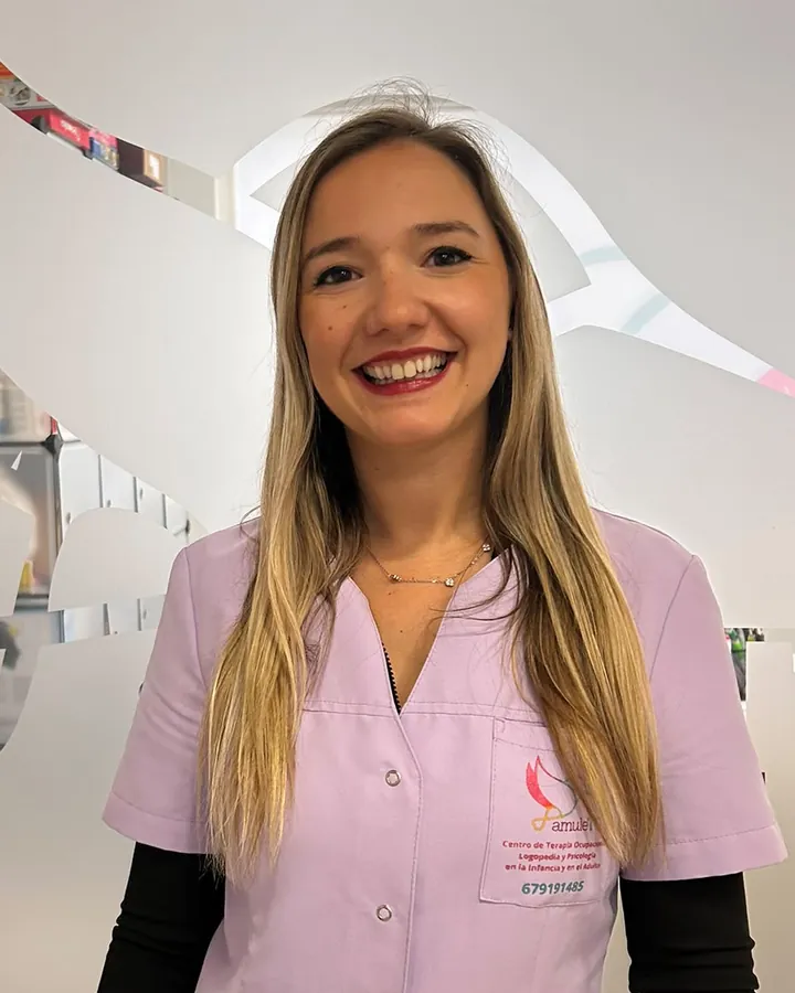 Lucía, sonriendo, con el uniforme lila del centro delante del cristal grabado con el logotipo de AmuleTO