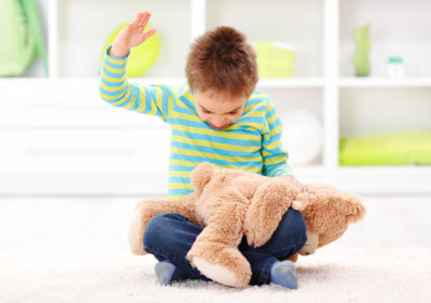 Niño sentado en el suelo levantando la mano sobre un peluche