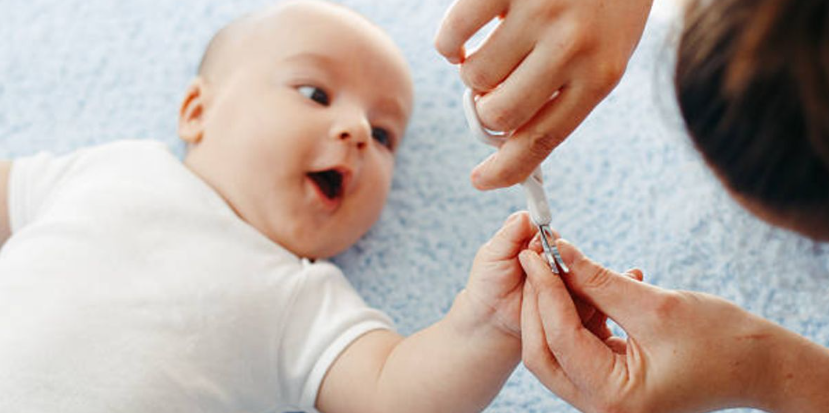 Adulto cortando las uñas a un bebé tumbado, que le mira con la boca abierta