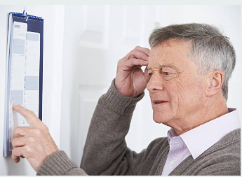 Hombre mayor mirando un calendario de pared con gesto de esfuerzo por recordar