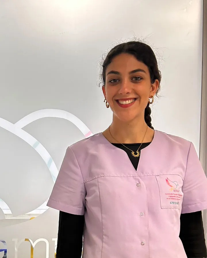 Rocío, sonriendo, con el uniforme lila del centro junto al cristal grabado con el logotipo de AmuleTO