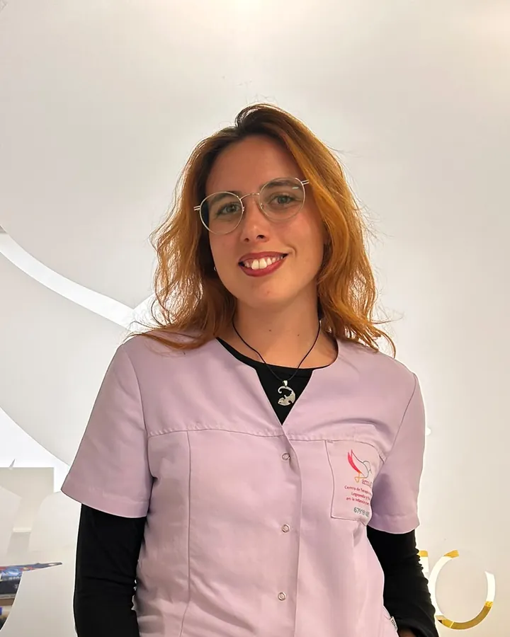 Sandra, con gafas y el uniforme lila del centro, delante del cristal grabado con el logotipo de AmuleTO