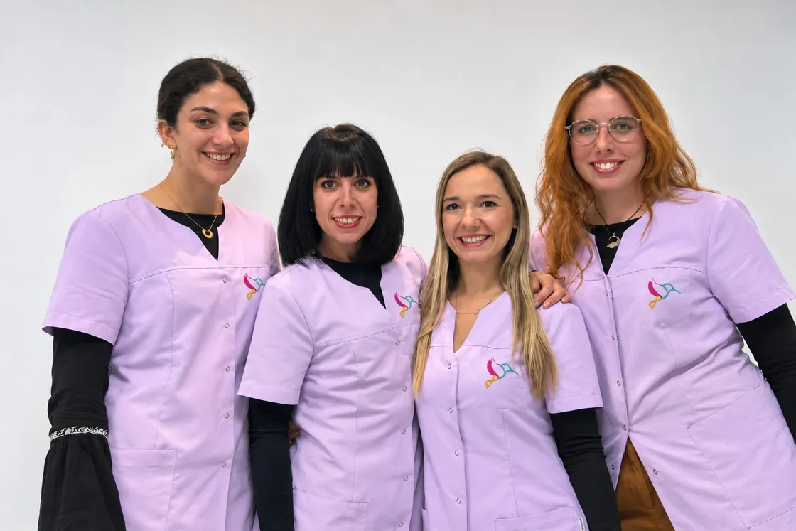 Las cuatro profesionales del equipo de AmuleTO con el uniforme lila del centro, sonriendo delante de una pared blanca